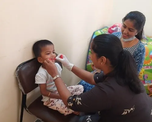 A therapist doing an oral placement exercise with a toddler while a parent watches